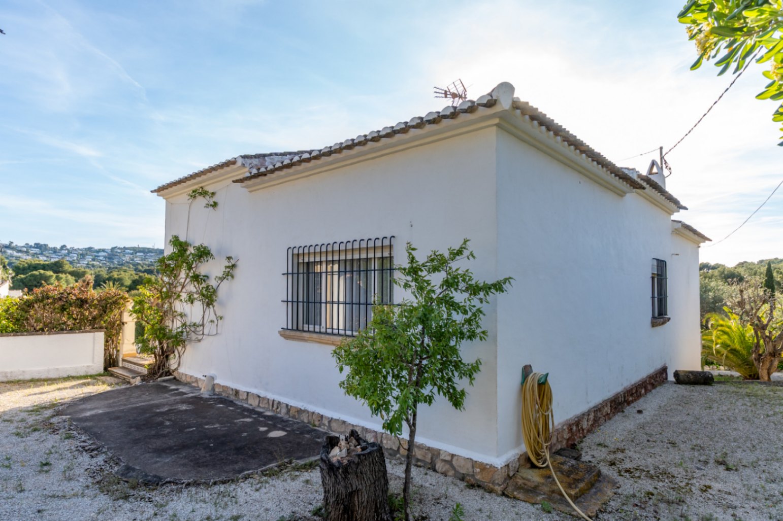 Vue extérieure de la façade blanche avec soubassement en pierre, toiture en tuiles traditionnelles et fenêtres équipées de grilles de sécurité en fer forgé.