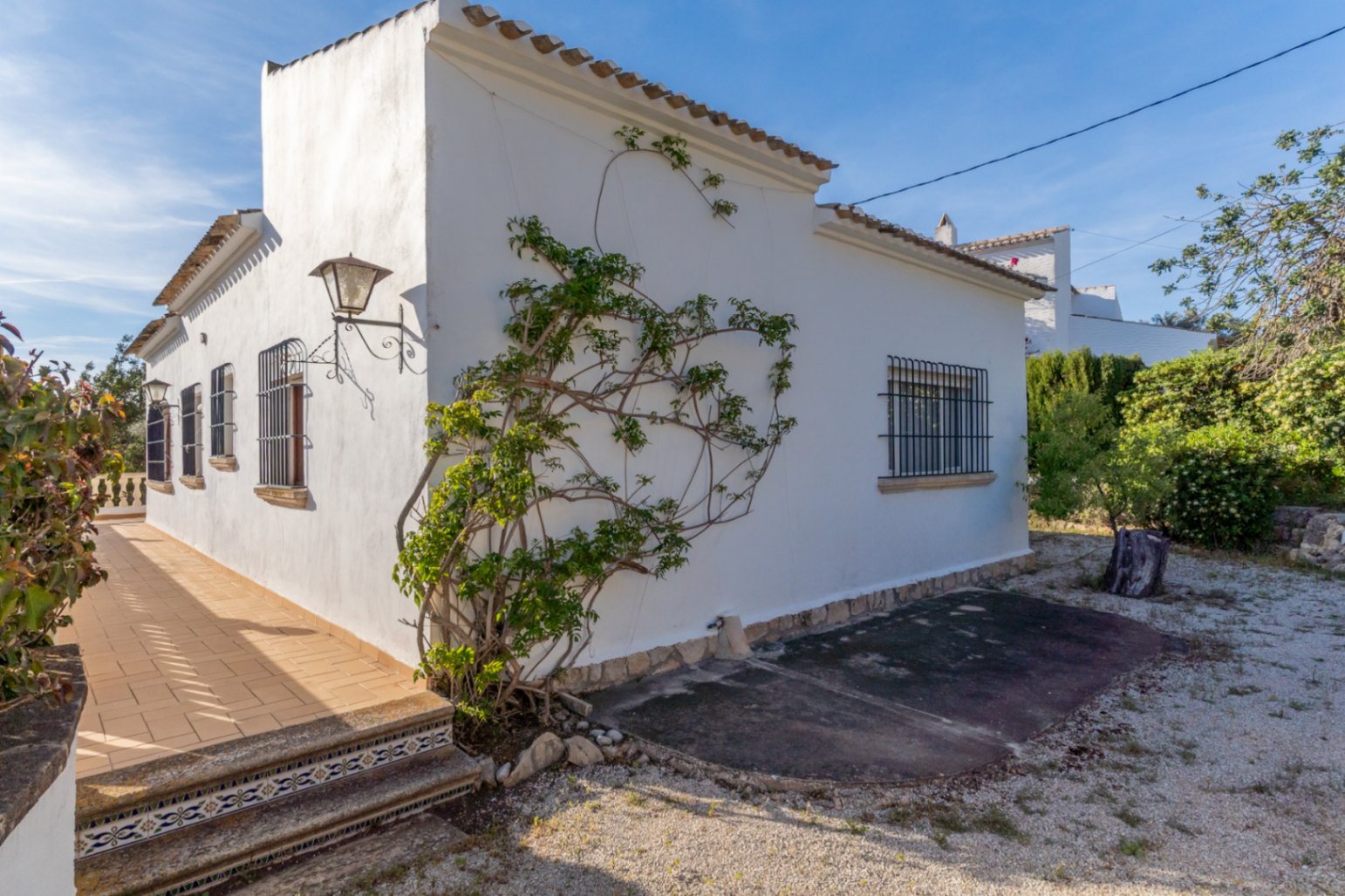 Vue extérieure de la villa avec façades blanches, fenêtres à barreaux en fer forgé et terrasse latérale aux marches ornées de carreaux de céramique traditionnels.