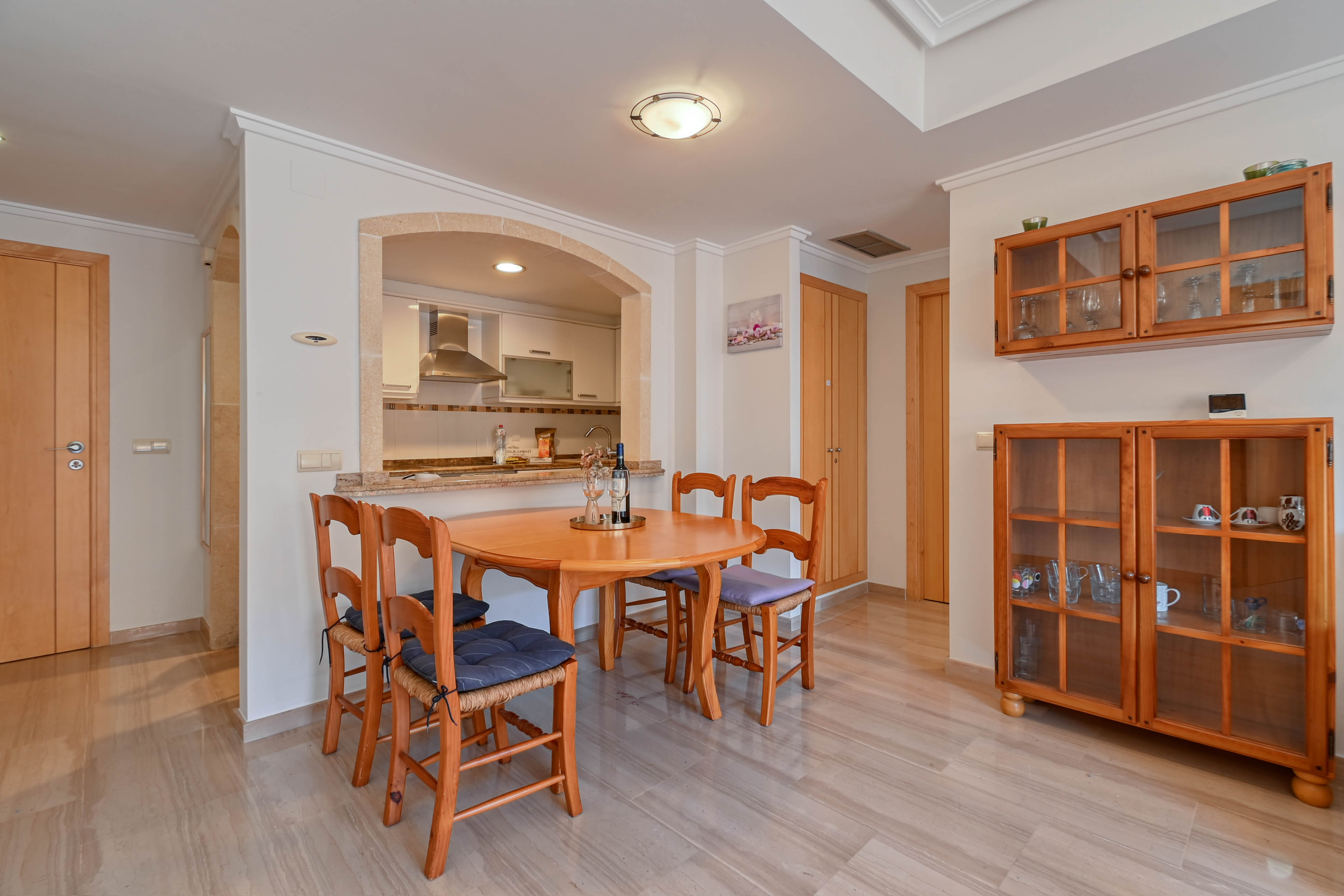 Coin repas avec table en bois et chaises, ouvert sur la cuisine par une arche en pierre et doté d'un sol en marbre poli.
