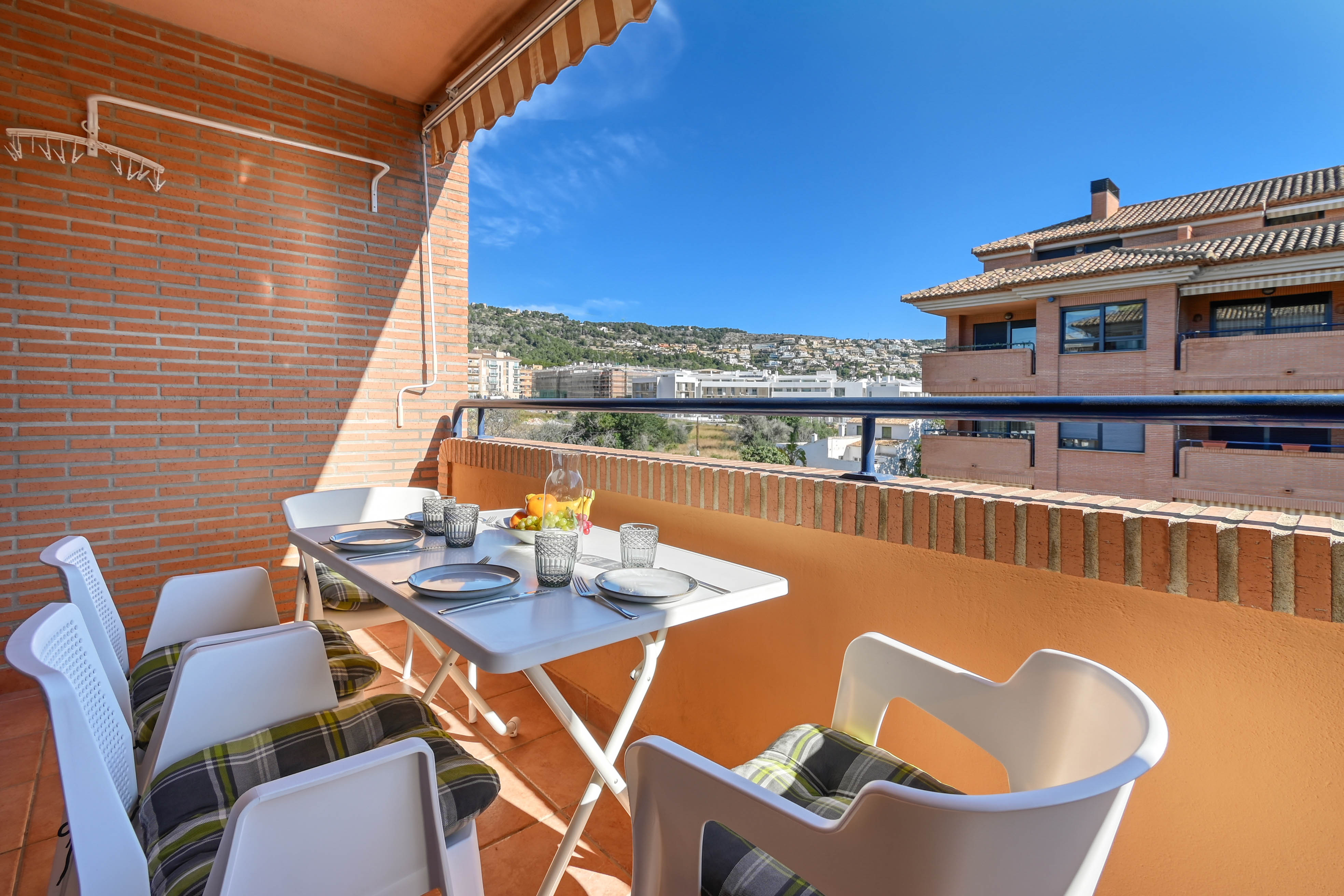 Terrasse privée équipée d'une table extérieure, d'un store banne et de murs en briques. Elle offre une vue dégagée sur les collines et le quartier résidentiel.