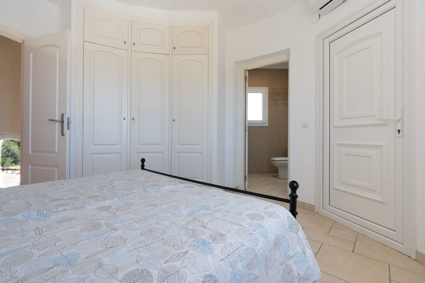 Chambre lumineuse avec placards intégrés blancs, sol en grès cérame et accès direct à une salle de bains attenante carrelée.
