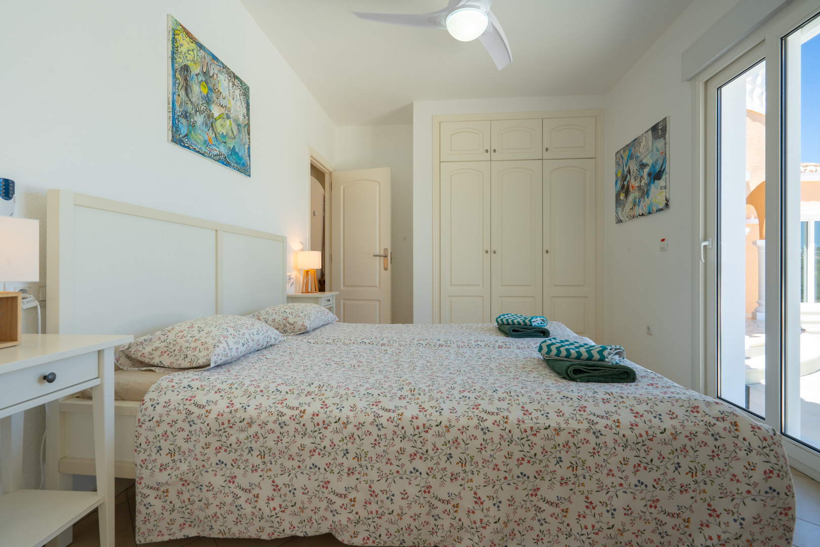 Chambre lumineuse avec placards intégrés, ventilateur de plafond et accès direct à l'extérieur par des portes coulissantes en PVC à double vitrage.