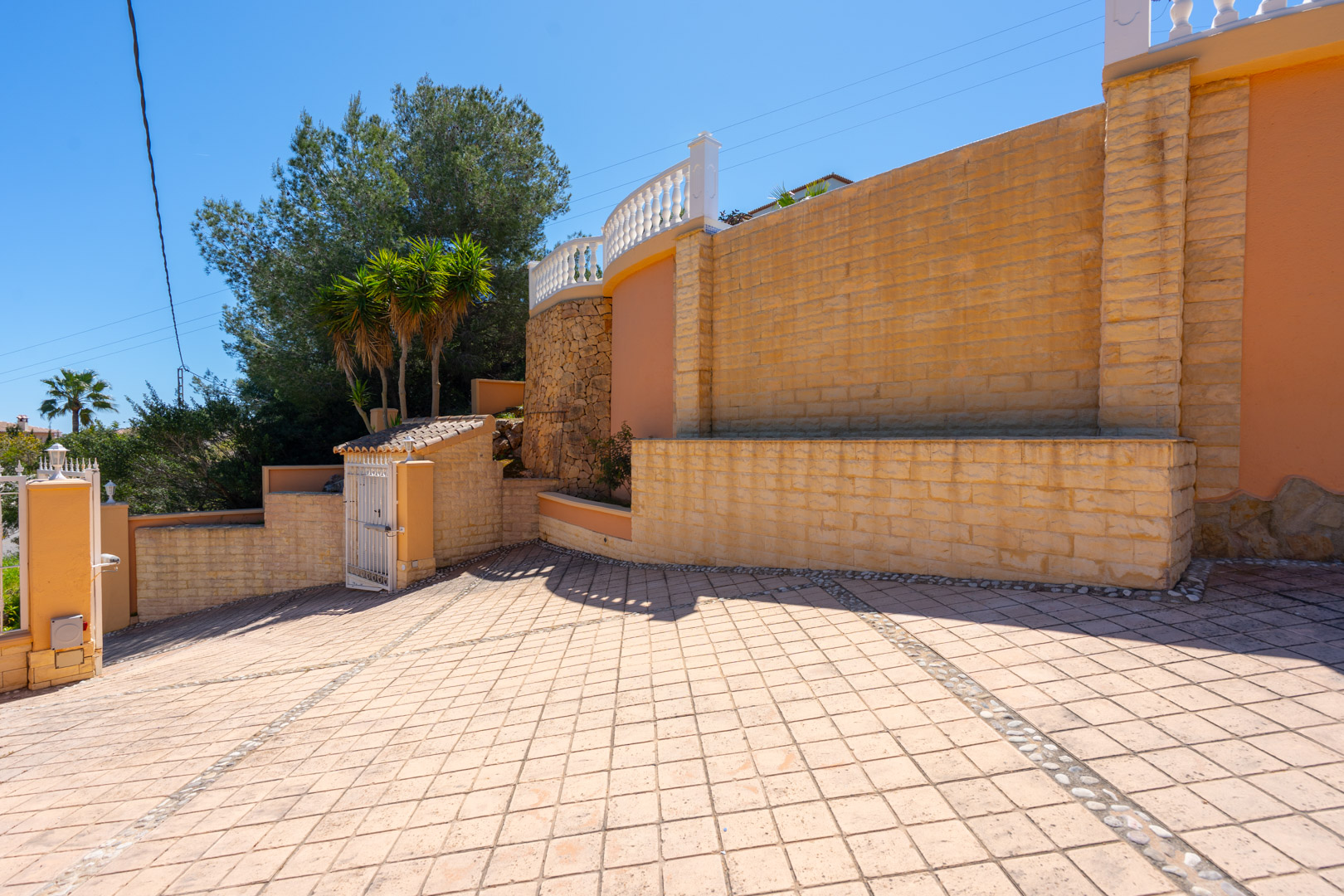 Entrée principale avec une large allée pavée en losanges, des murs de soutènement en pierre naturelle et une terrasse supérieure avec balustrade blanche.