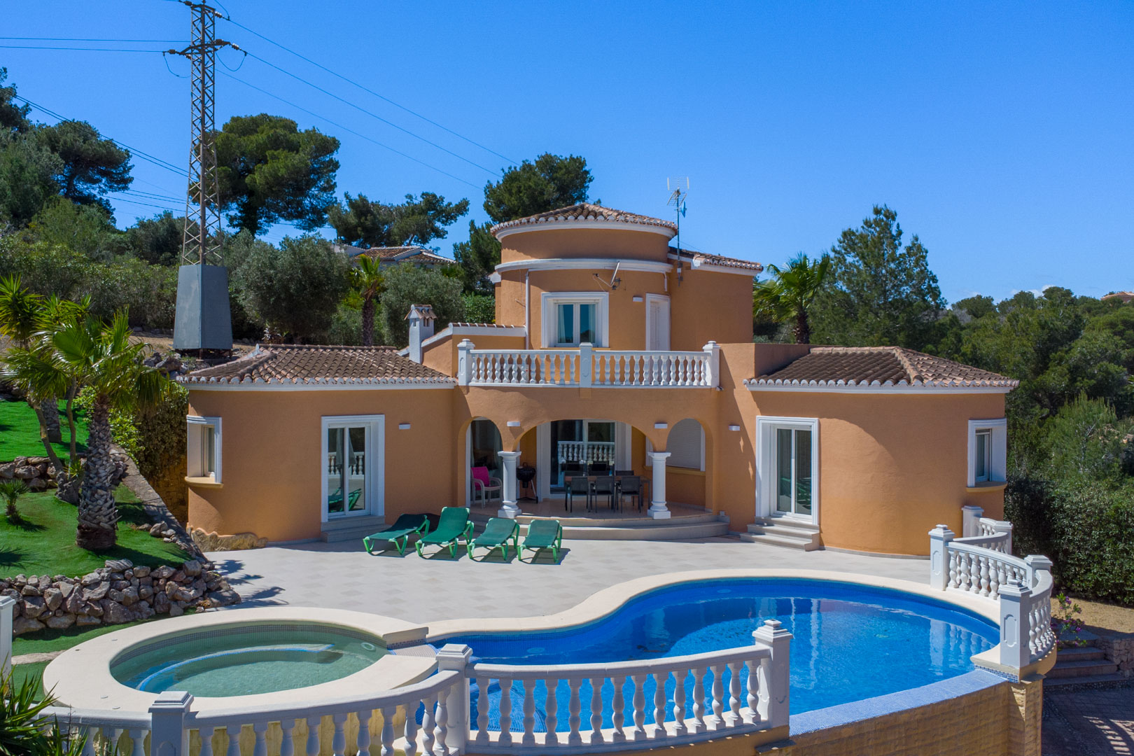 Extérieur de la villa avec piscine de forme libre, jacuzzi intégré et grande terrasse. La façade méditerranéenne est ornée de balustrades blanches et d'un porche couvert.