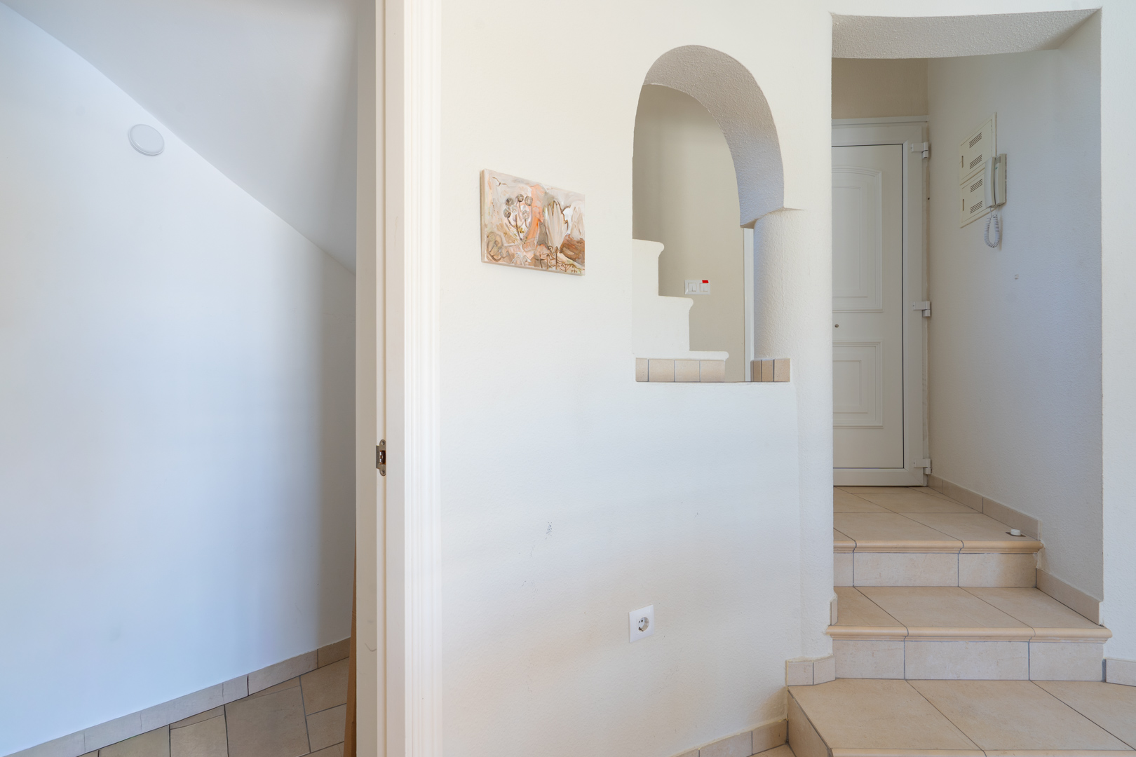 Hall d'entrée avec escalier intérieur, carrelage en céramique neutre et une ouverture murale en arche de style méditerranéen.