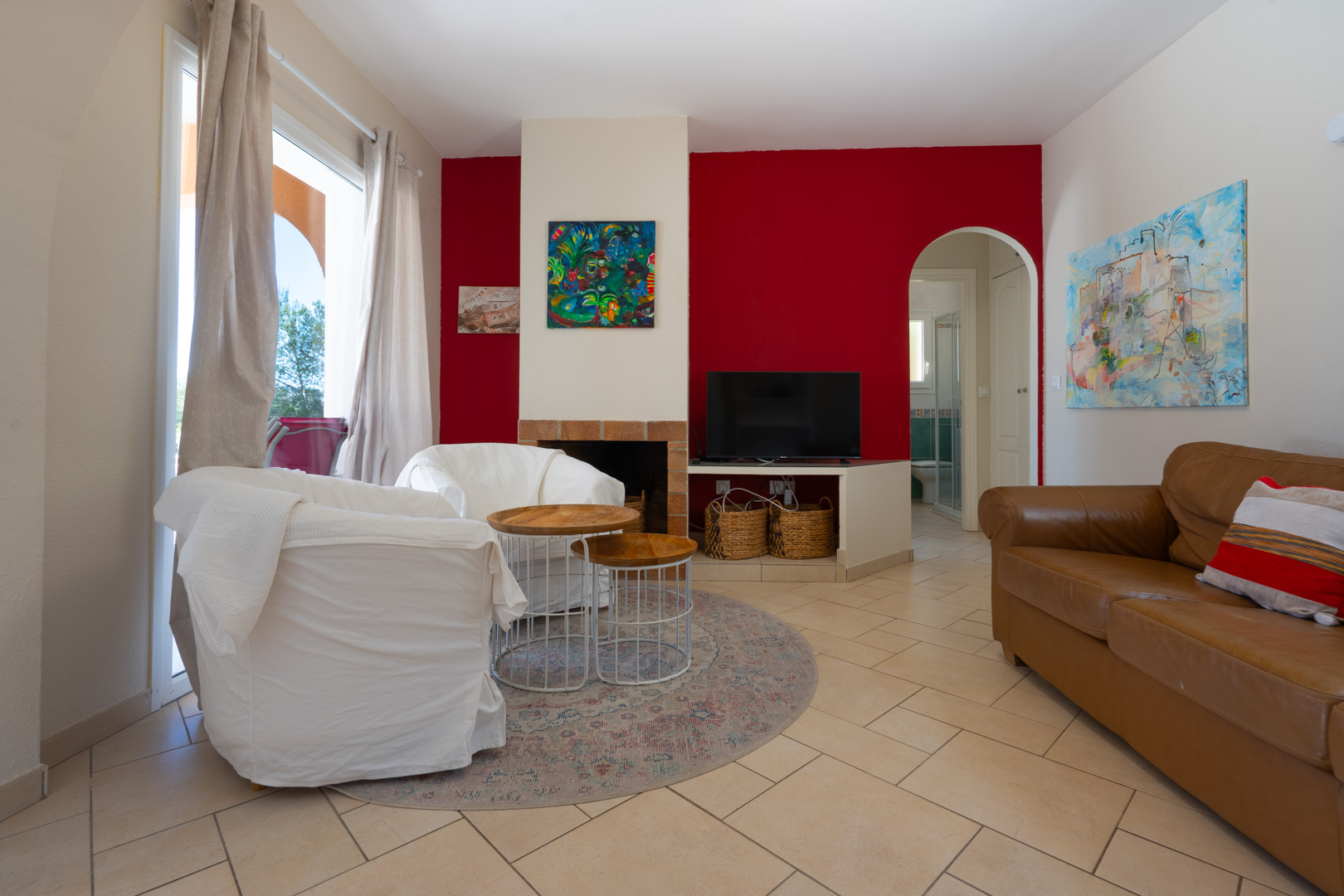 Salon avec mur d'accent rouge, cheminée intégrée et passage voûté. Comprend un sol en carrelage, un canapé en cuir et une luminosité naturelle abondante.