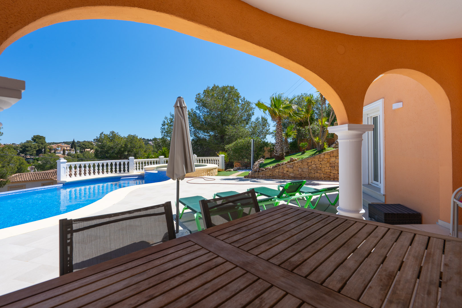 Terrasse couverte avec arches traditionnelles offrant une vue sur la piscine privée, l'espace solarium avec transats et le jardin méditerranéen paysagé.