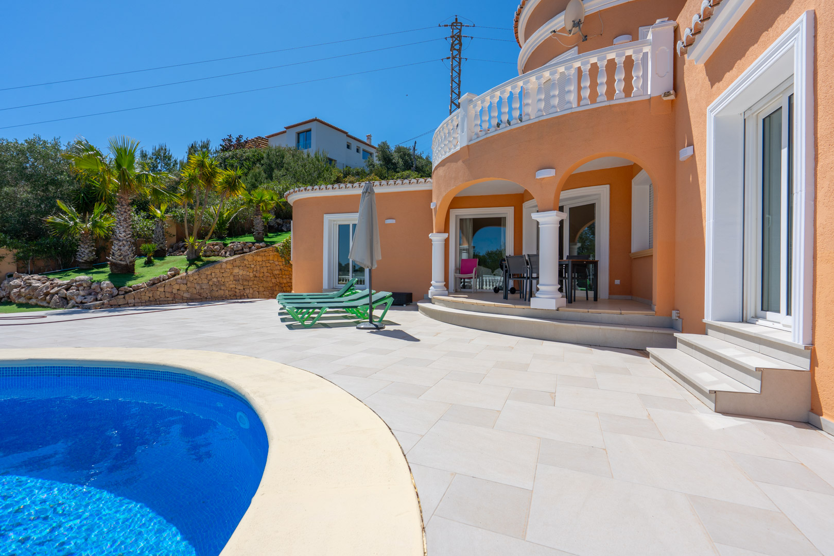 Terrasse extérieure avec piscine incurvée et porche à arches blanches. La façade ocre s'harmonise avec les balustrades classiques et un jardin méditerranéen soigné.
