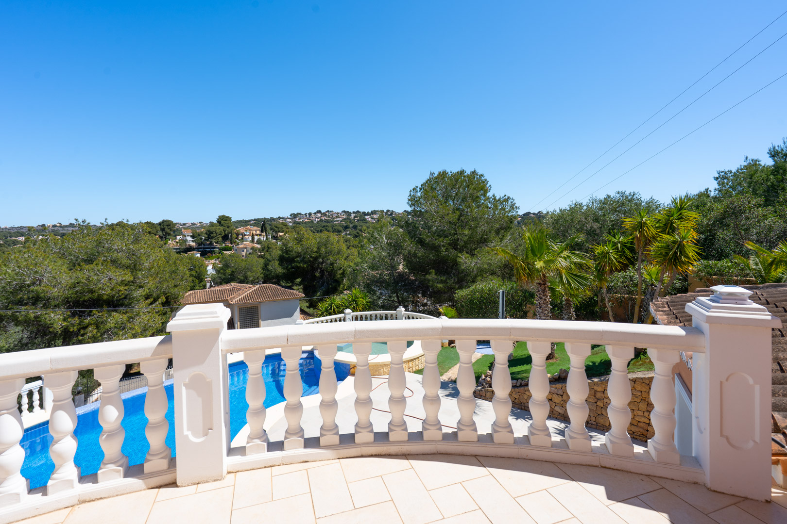 Terrasse supérieure avec balustrade classique en pierre blanche, offrant une vue sur la piscine privée, le jardin arboré et les collines environnantes.