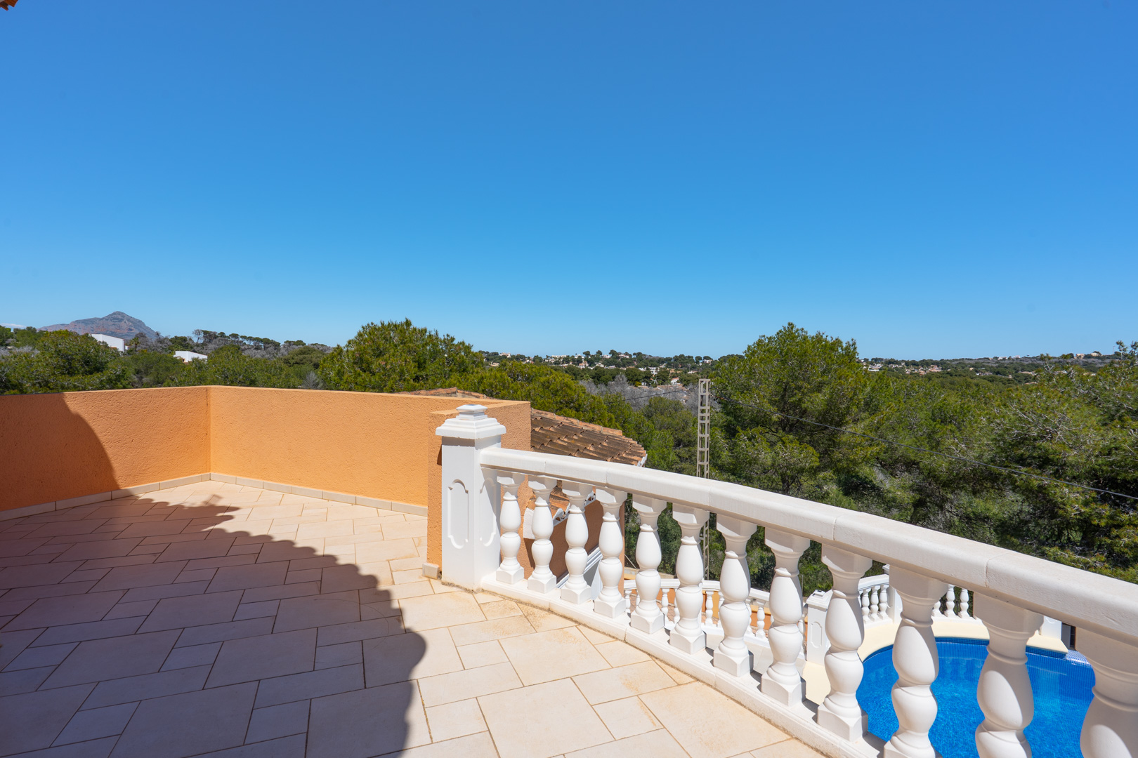Terrasse supérieure avec carrelage en céramique et balustrade blanche, offrant une vue sur la piscine privée et la végétation environnante.
