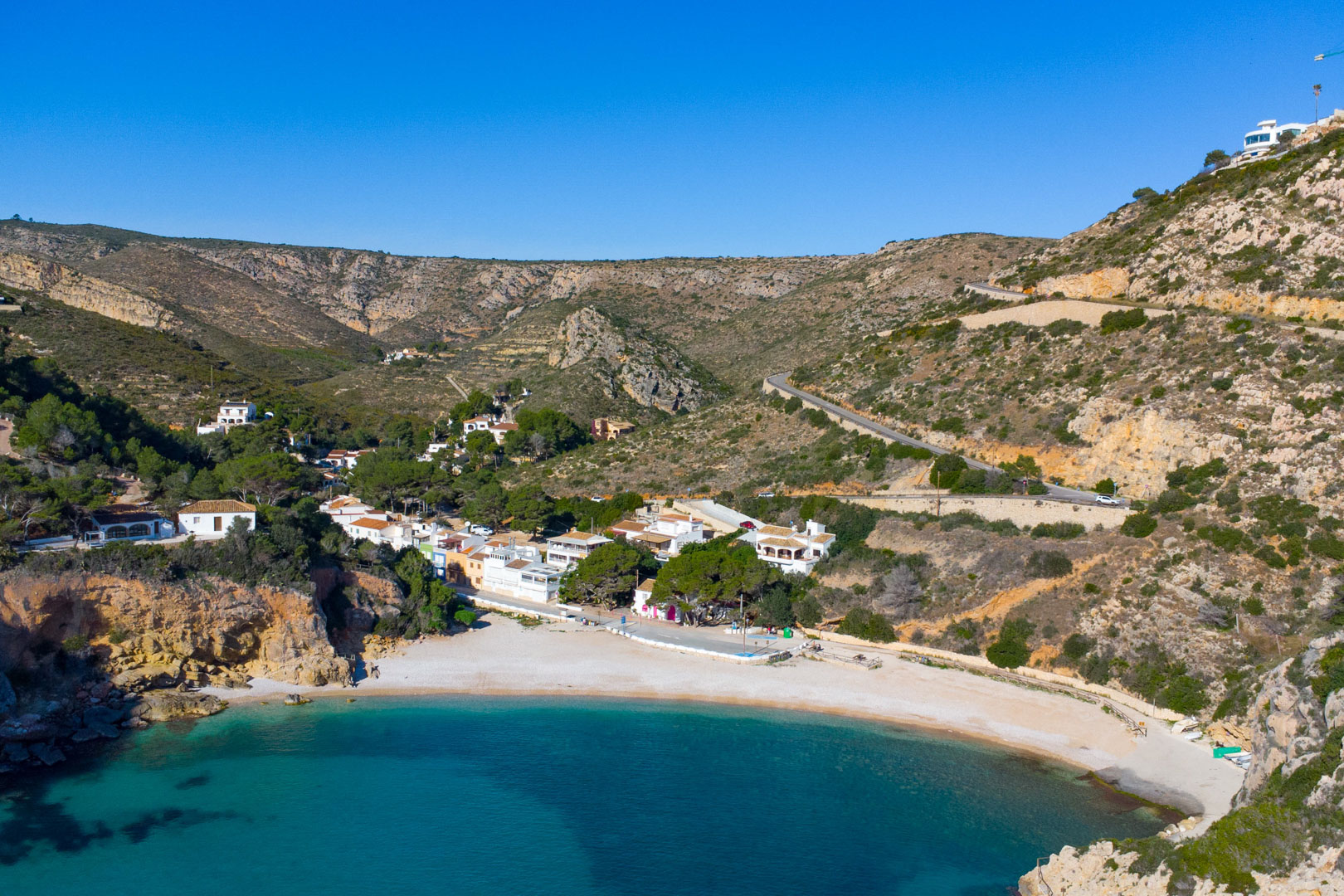 Vue aérienne de la Cala Granadella à Jávea, révélant des eaux turquoise, une plage de galets et des falaises escarpées entourant ce littoral préservé.