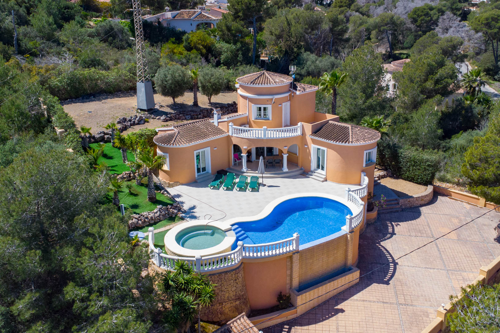 Vue aérienne de la villa méditerranéenne avec piscine de forme libre, jacuzzi intégré, grande terrasse pavée et architecture traditionnelle en terre cuite.