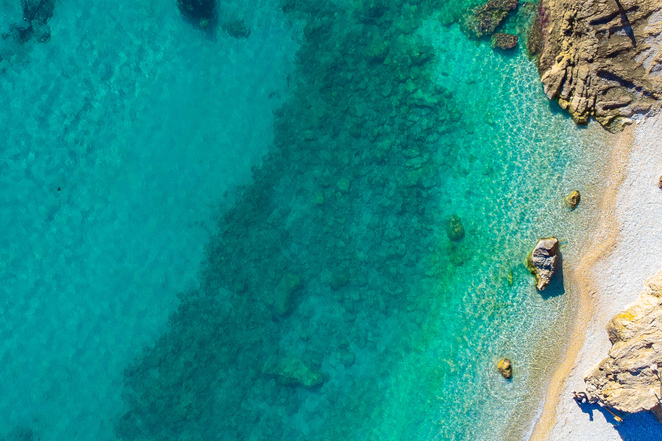 Vue aérienne du littoral de Jávea, révélant des eaux turquoise cristallines, des fonds marins rocheux et un rivage de galets naturels.