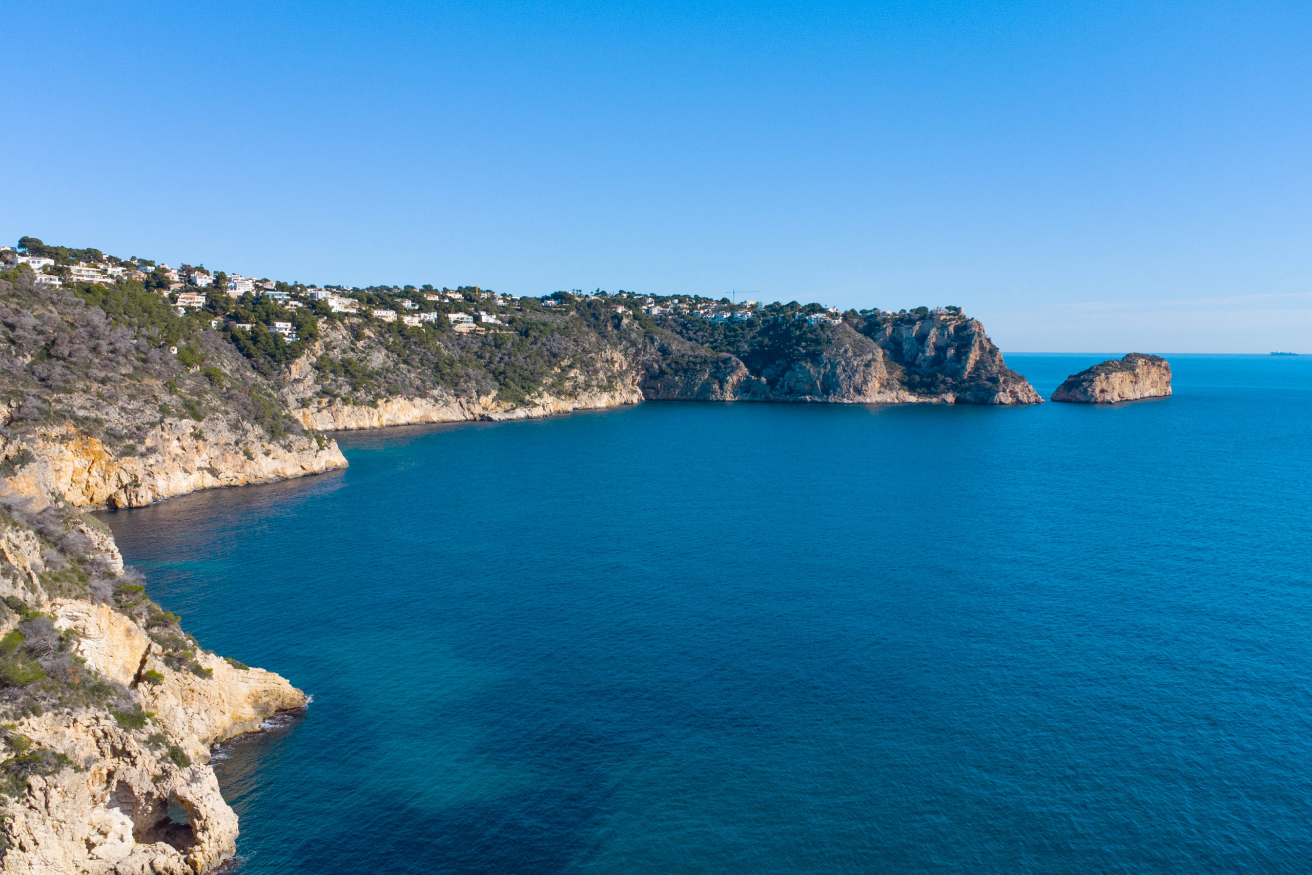 Vue panoramique sur les falaises de Jávea et la mer Méditerranée, illustrant le littoral rocheux escarpé et les résidences situées en bord de mer.
