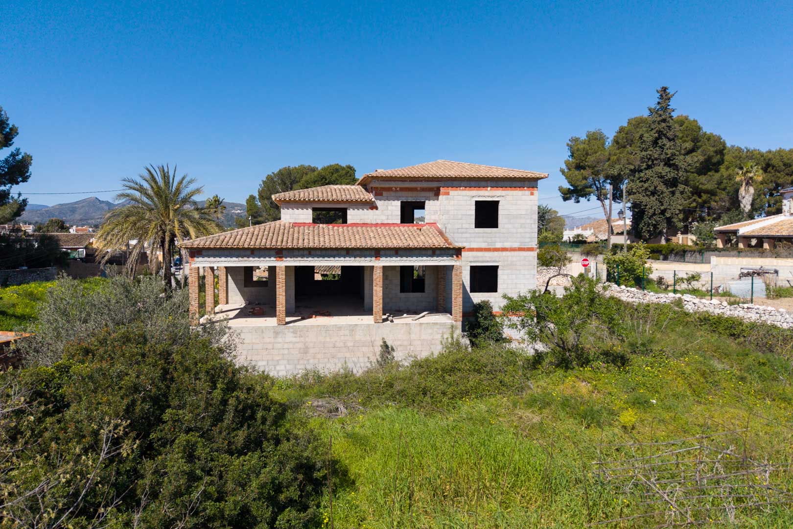 Structure de maison individuelle sur deux niveaux avec toiture en tuiles, larges porches soutenus par des piliers en briques et vues dégagées sur la nature environnante.