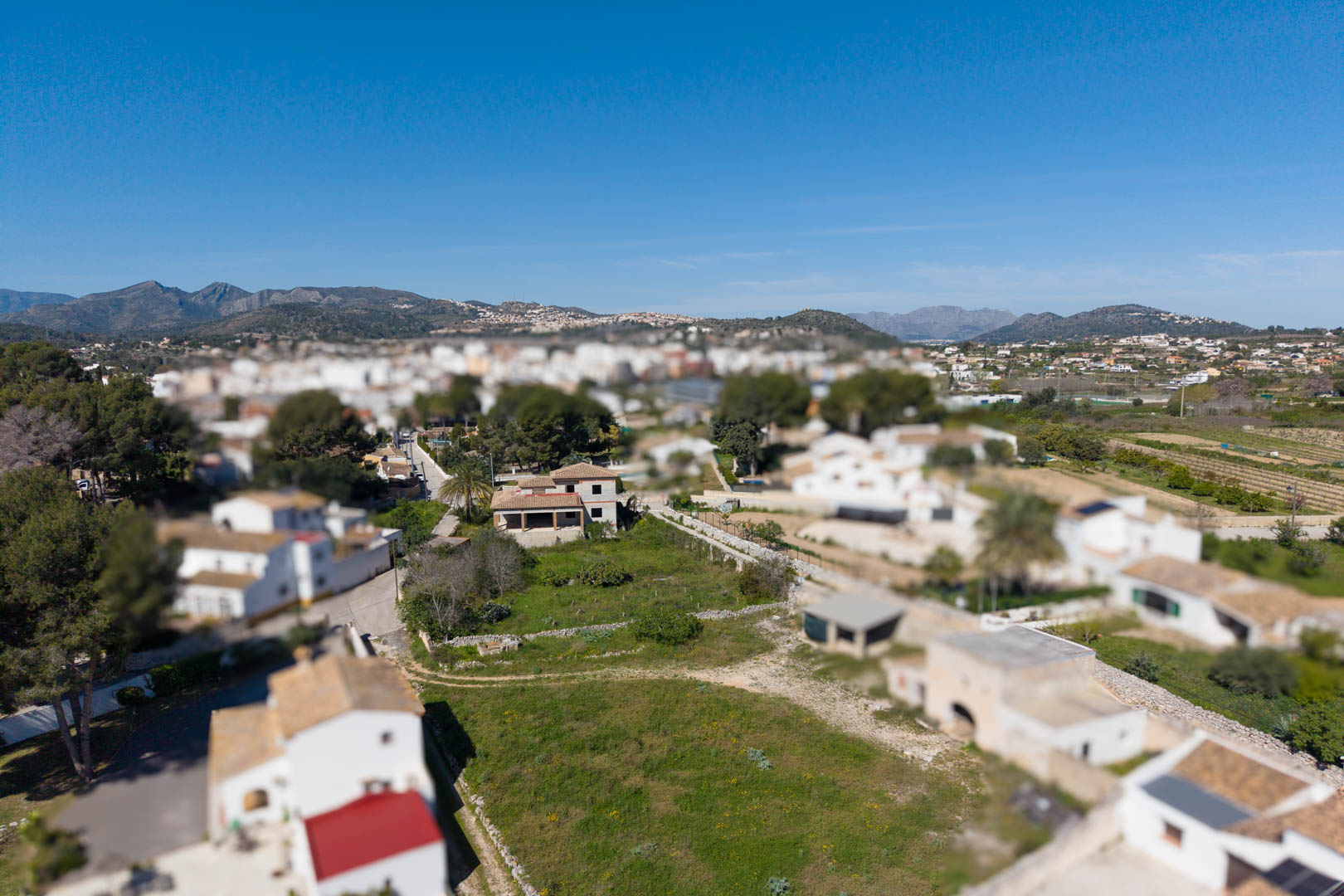 Vue aérienne de la parcelle de 1800 m² comprenant la structure de la maison principale et des bâtiments annexes, avec les montagnes en arrière-plan.