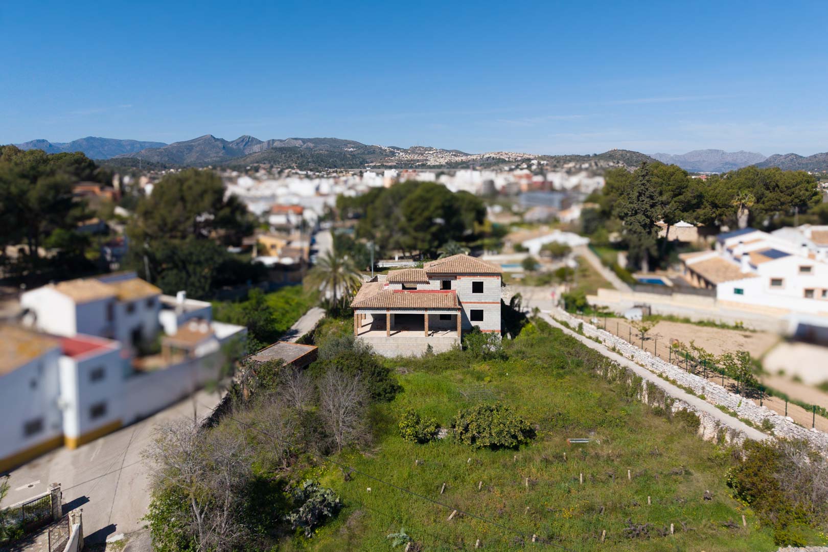 Vue aérienne de la structure en construction avec toit en tuiles, située sur un vaste terrain de 1800 m² offrant une vue dégagée sur les montagnes environnantes.