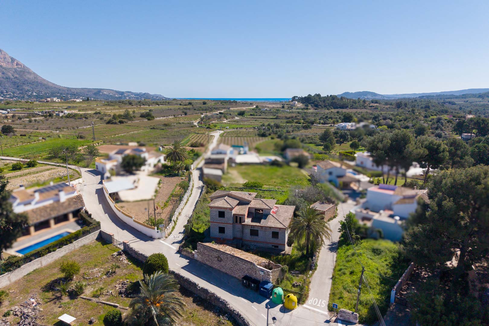 Vue aérienne de la structure inachevée avec toiture en tuiles, située dans un environnement rural offrant des vues sur le Montgó et la mer à l'horizon.
