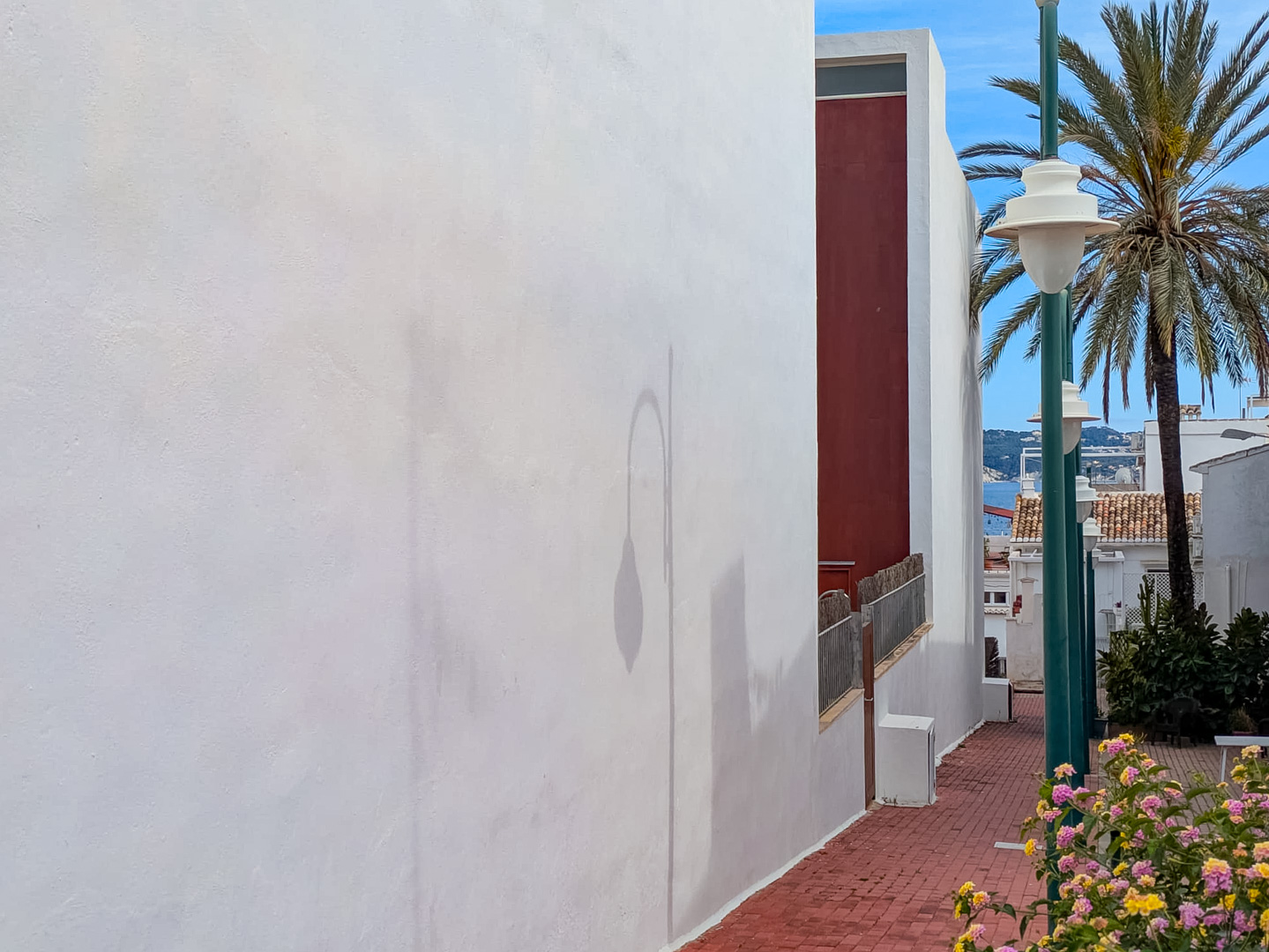Extérieur du bâtiment avec façade blanche et chemin piétonnier en briques offrant une vue partielle sur la mer et la végétation.