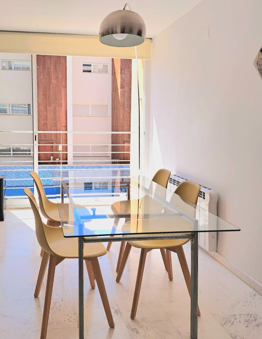 Salle à manger lumineuse avec table en verre, chaises de style nordique et sol en marbre, offrant une vue sur la piscine via la grande baie vitrée.