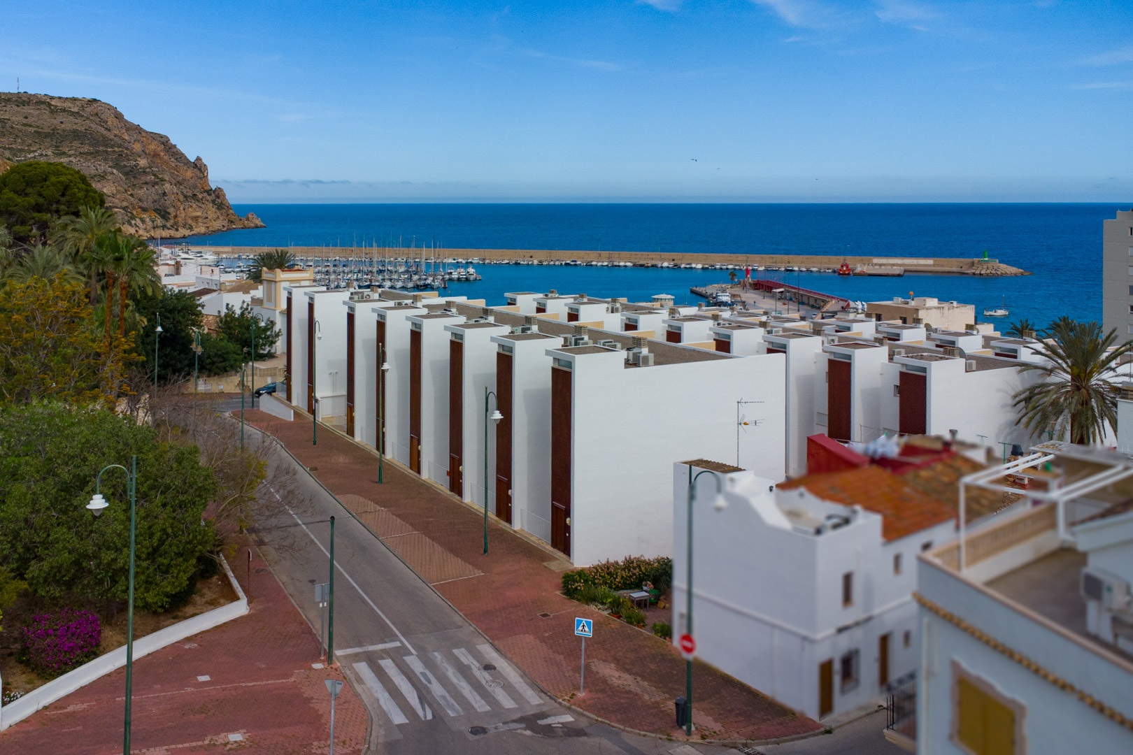 Vue panoramique sur le port de Jávea et la mer Méditerranée, mettant en avant l'architecture moderne blanche et la proximité directe du front de mer.