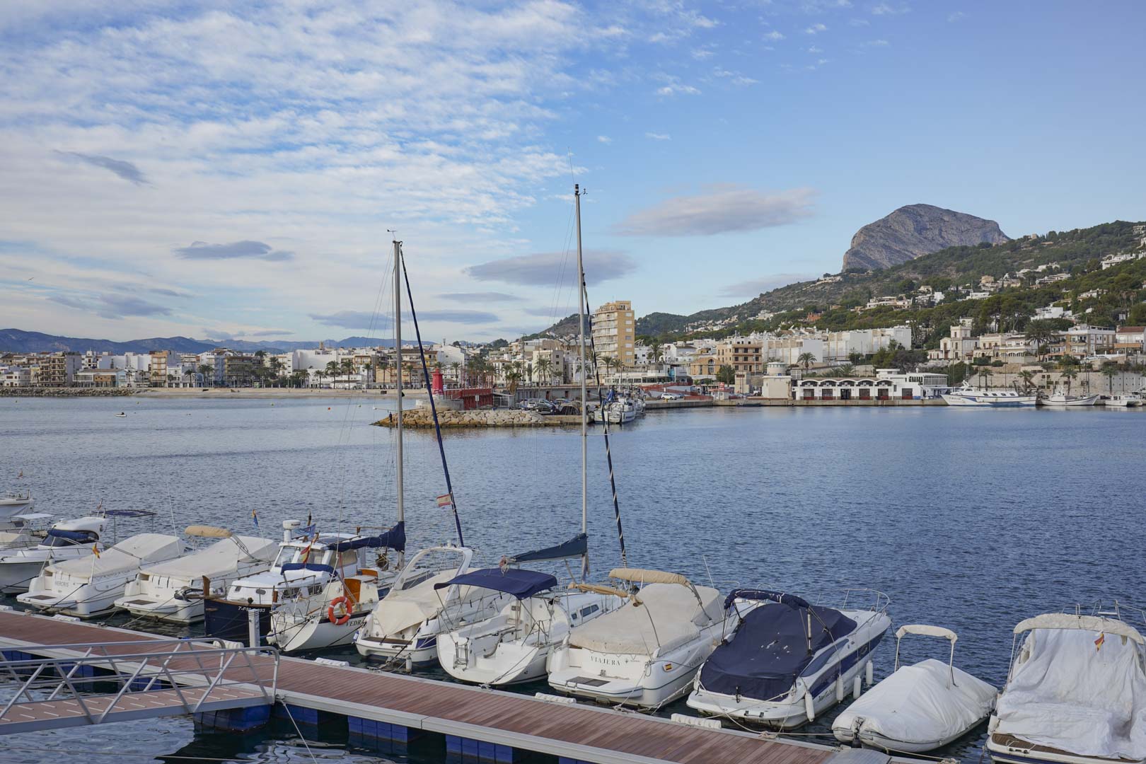 Vue panoramique sur le port de plaisance de Jávea, illustrant les bateaux à quai et la silhouette du Montgó s'élevant au-dessus de la ville.