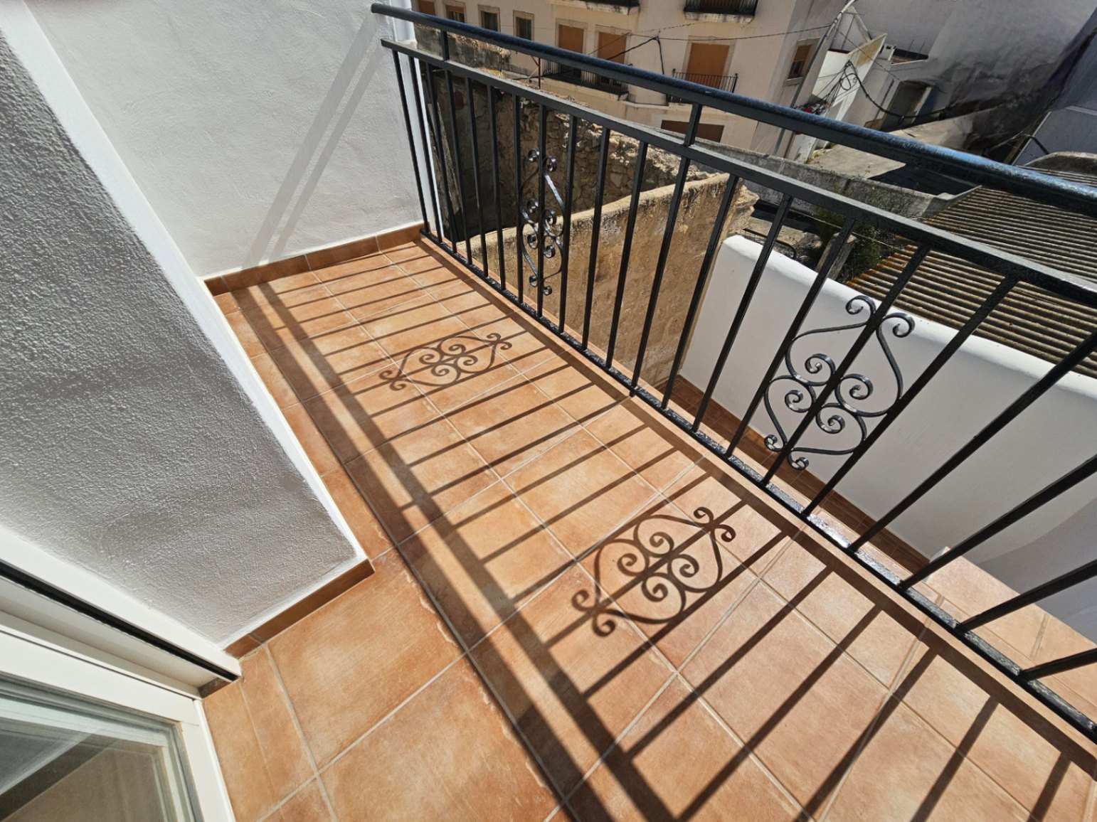 Balcon avec revêtement de sol en terre cuite et garde-corps en fer forgé noir ornemental, offrant une vue sur les maisons traditionnelles du village.