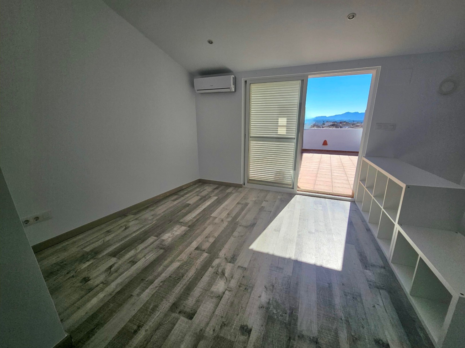 Bureau lumineux avec parquet, climatisation et accès direct à une terrasse privée offrant une vue panoramique sur les montagnes.