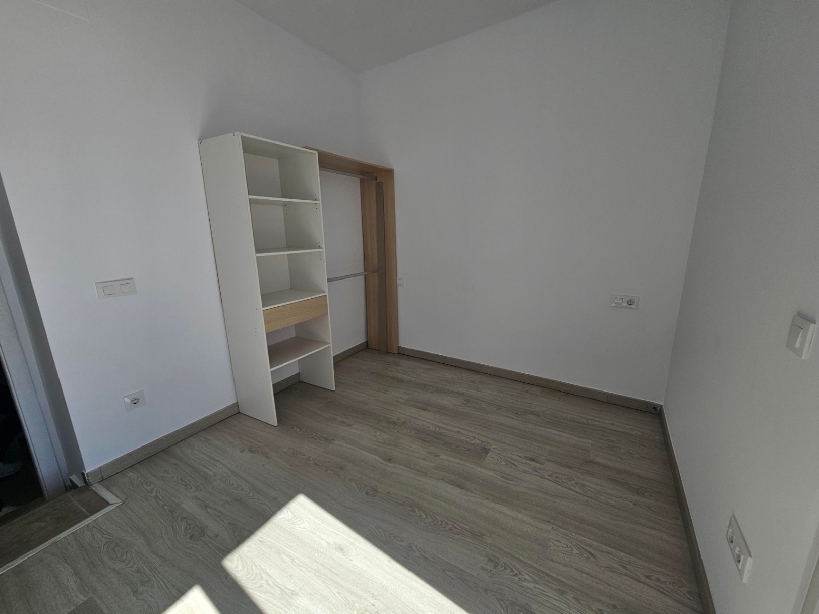 Chambre avec revêtement de sol gris effet bois, murs blancs et un système de rangement ouvert modulable alliant étagères blanches et bois clair.