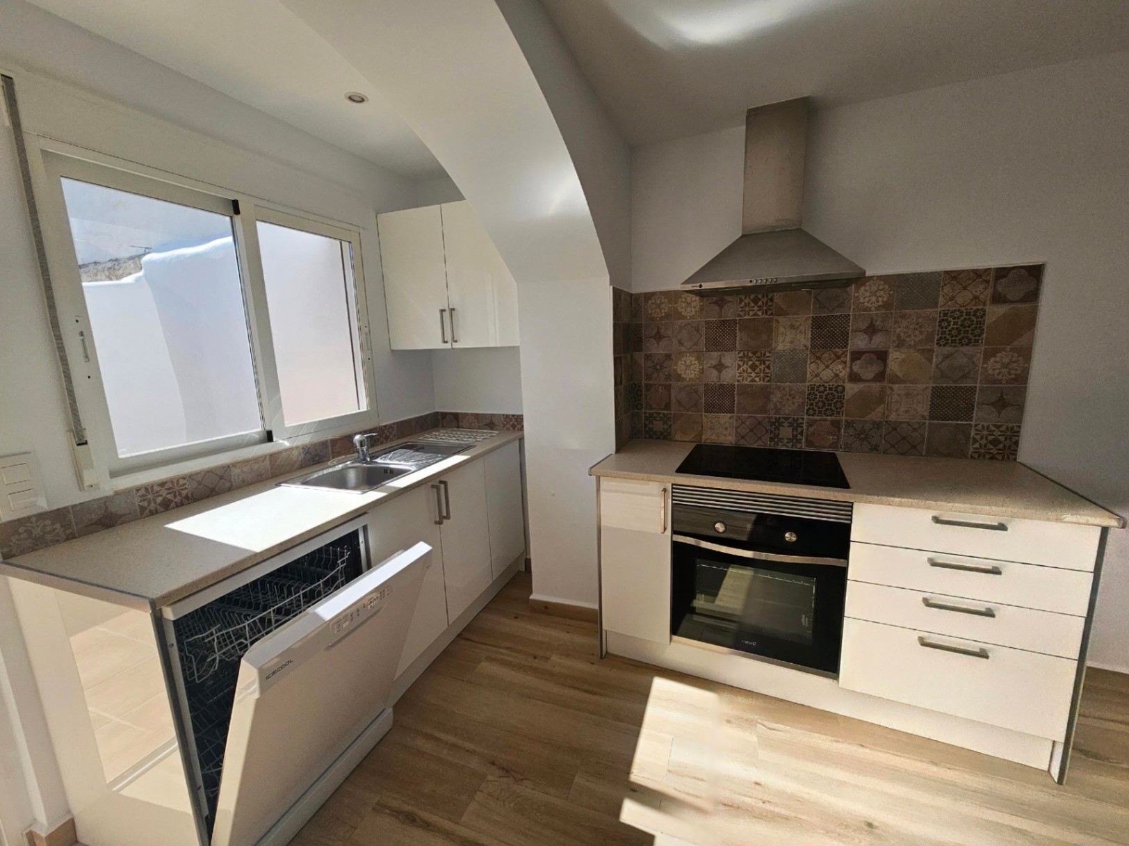 Cuisine moderne rénovée avec meubles blancs, crédence en carreaux de ciment et électroménager intégré. Le sol en bois apporte une touche chaleureuse à l'espace.