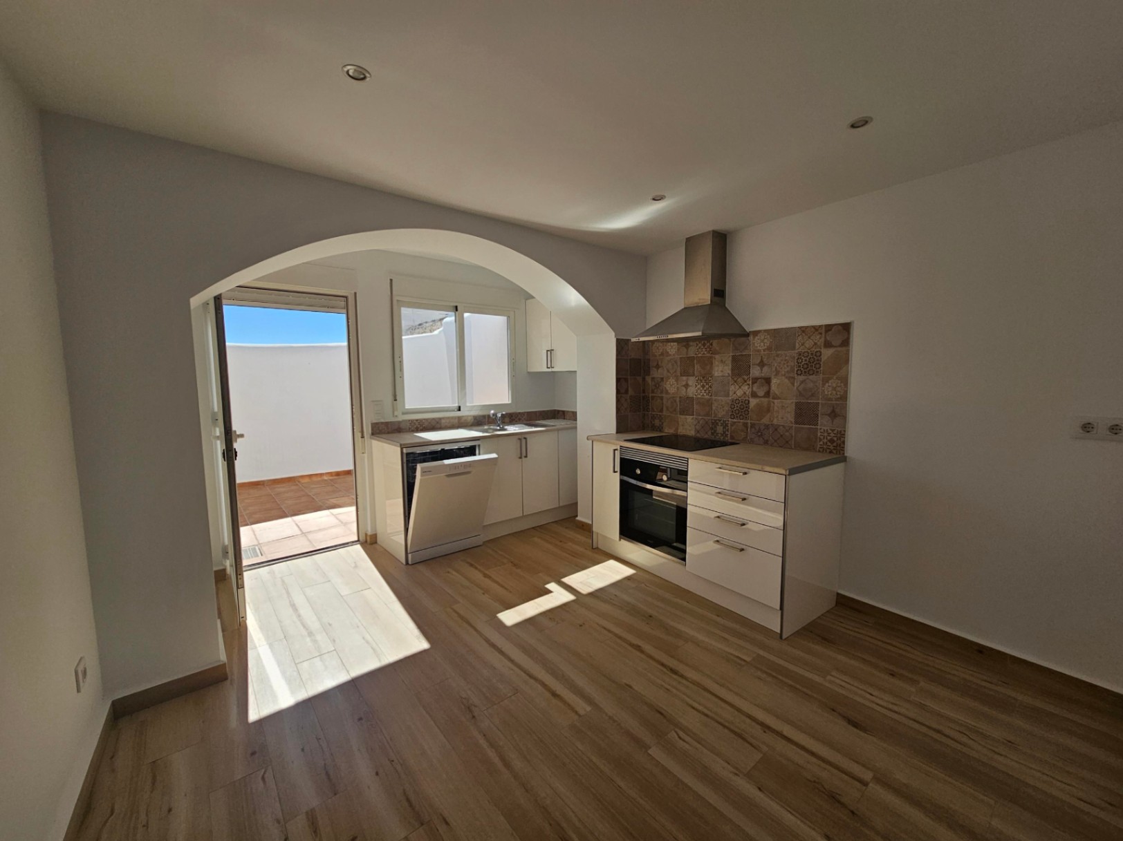Cuisine ouverte rénovée avec meubles blancs, crédence en carreaux de ciment et accès direct au patio extérieur par une ouverture en arche.