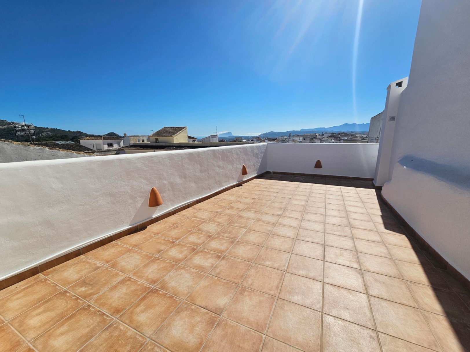 Terrasse sur le toit avec carrelage en terre cuite, murs blanchis à la chaux et vue panoramique sur le village, les montagnes et la mer.