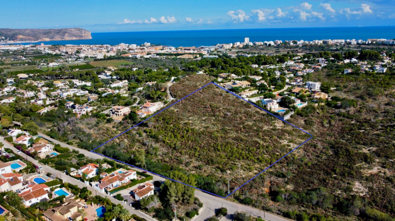 Vue aérienne de la parcelle de 17 272 m² à Jávea, délimitée en bleu, entourée de villas résidentielles avec une perspective dégagée sur la mer Méditerranée.