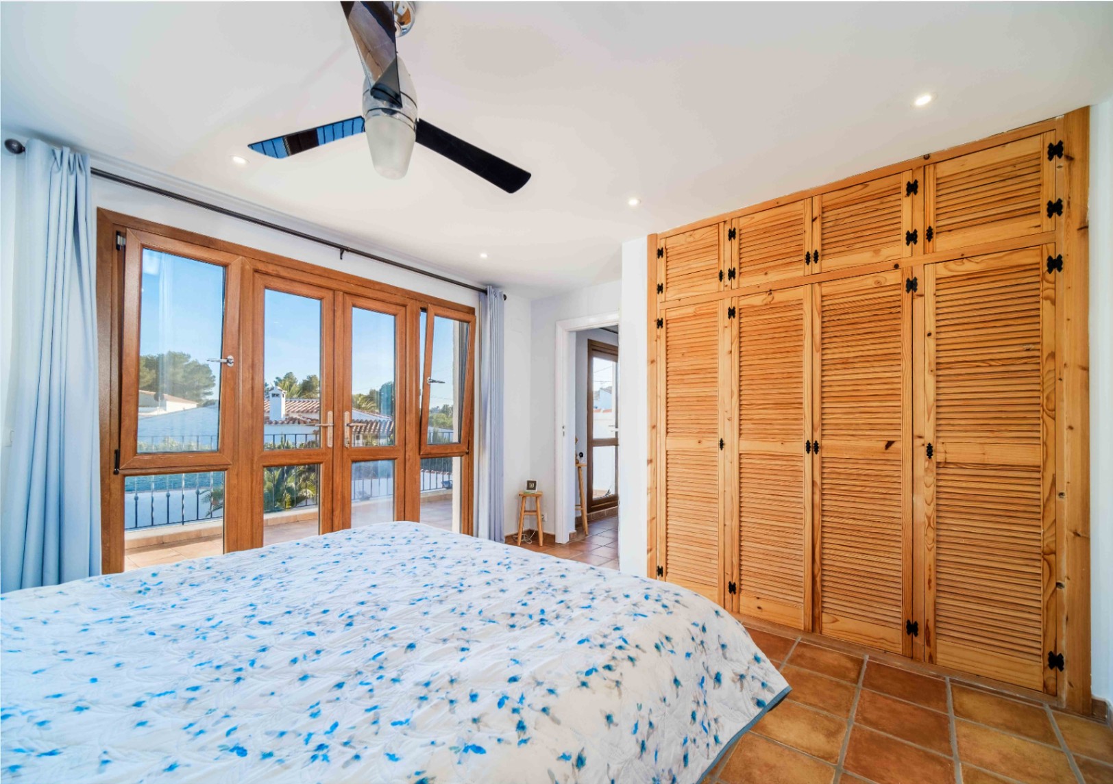 Chambre avec placards en bois intégrés, sol en terre cuite et grandes portes-fenêtres ouvrant sur une terrasse privée.