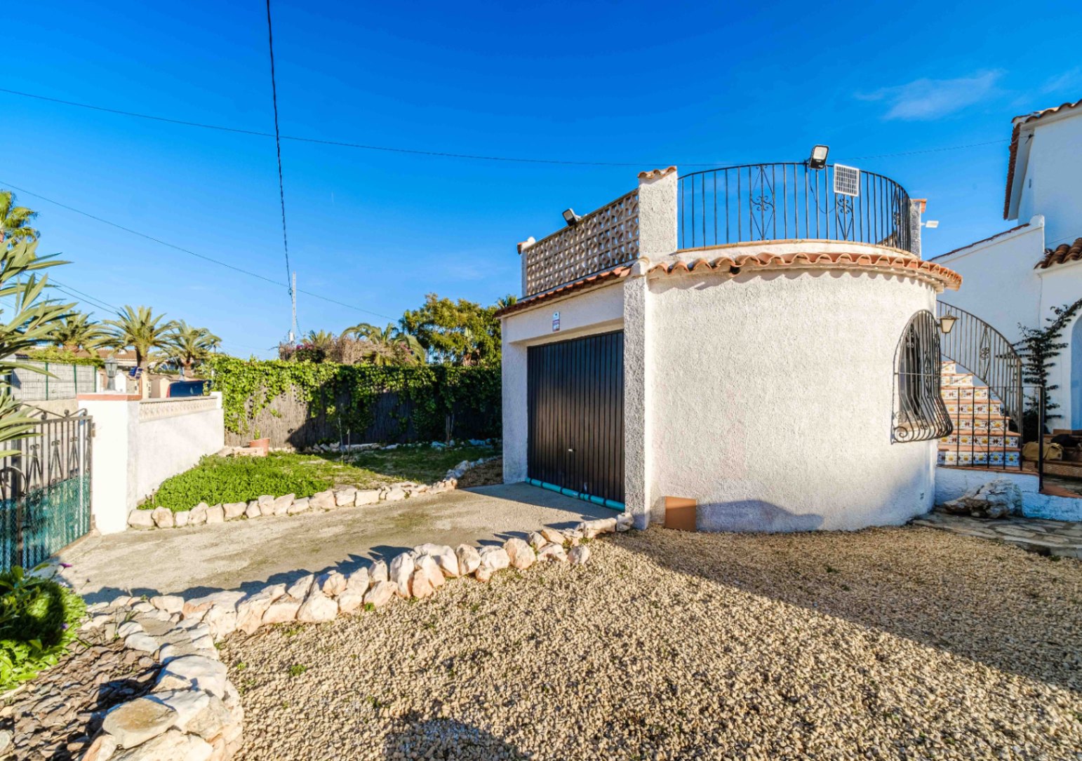 Garage privé avec porte noire et terrasse sur le toit avec garde-corps en fer forgé. L'extérieur dispose d'une allée en gravier et de bordures en pierre naturelle.
