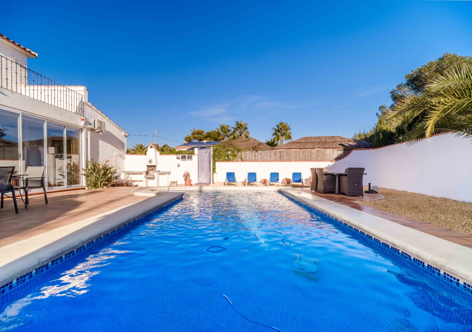Piscine rectangulaire en mosaïque bleue entourée d'une terrasse en terre cuite, avec barbecue intégré, coin repas extérieur et bains de soleil.