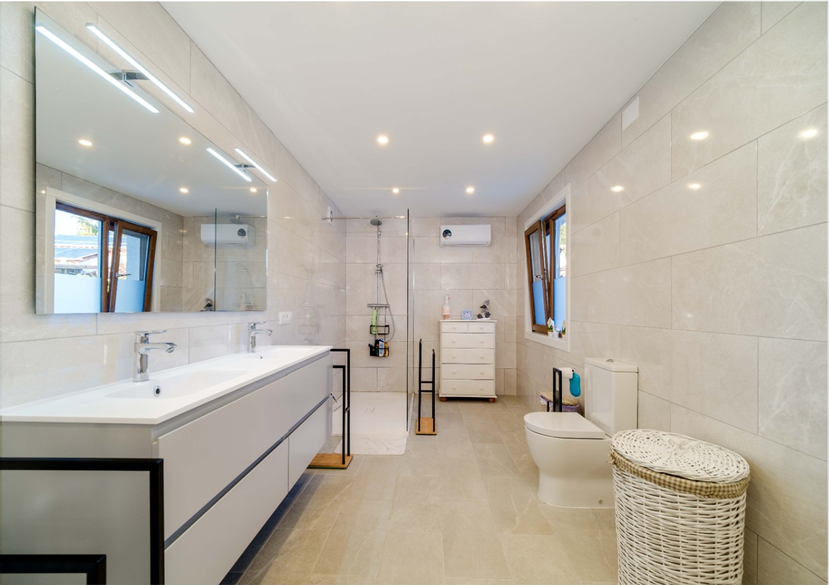 Salle de bain moderne avec double vasque, meuble gris suspendu, douche à l'italienne avec paroi vitrée et carrelage mural en grès cérame aux tons beiges.