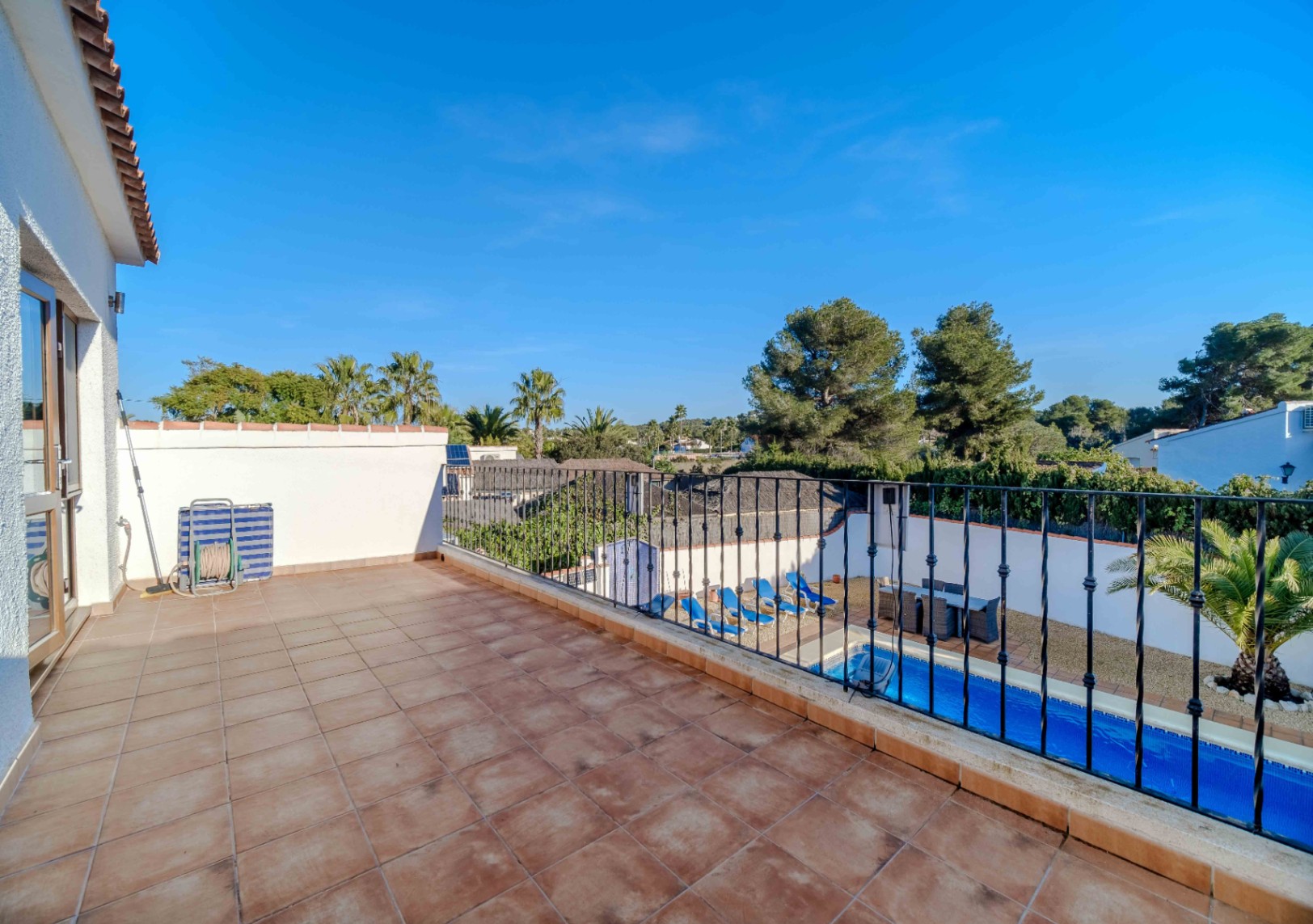 Terrasse surélevée avec carrelage en terre cuite et garde-corps en fer forgé, offrant une vue sur la piscine et la végétation environnante.
