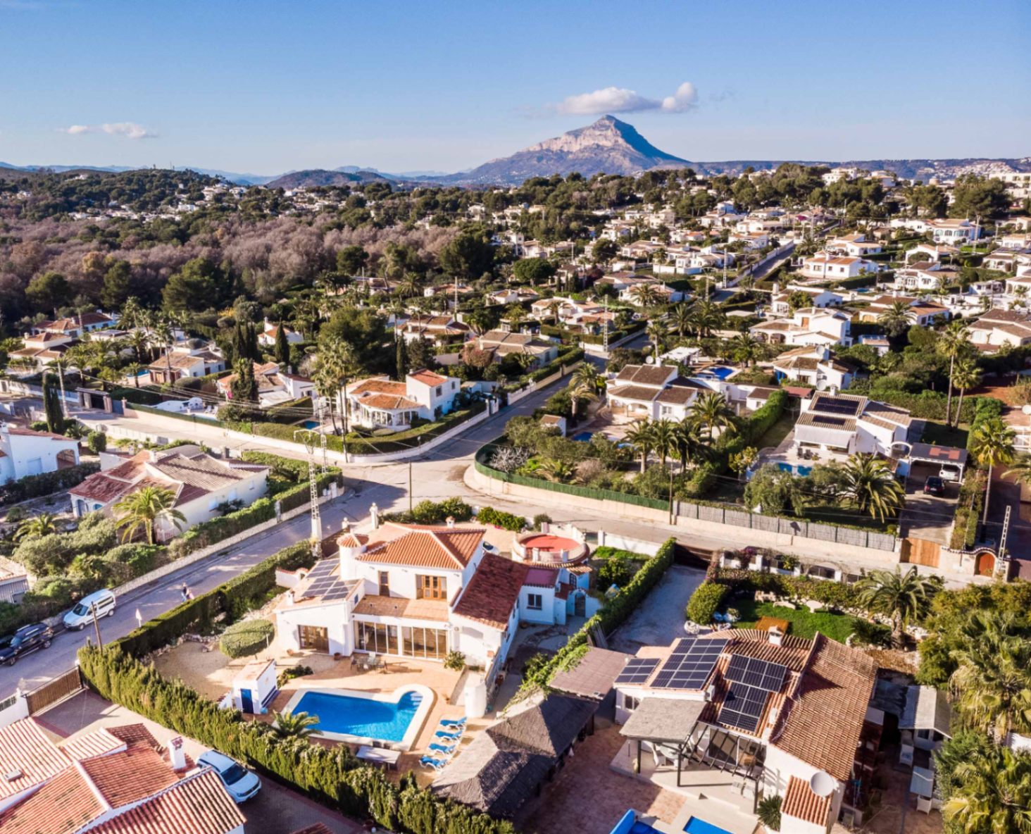 Vue aérienne de la villa à Costa Nova Pla, mettant en valeur la piscine, les panneaux solaires et le massif du Montgó à l'horizon.