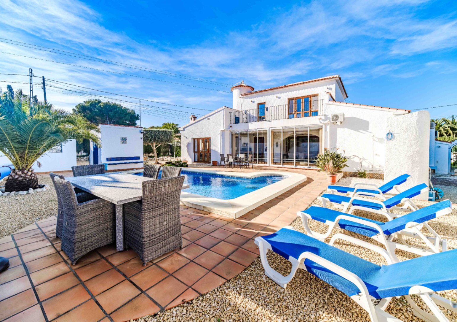 Vue extérieure de la villa avec piscine, espace dînatoire et bains de soleil, mettant en valeur l'architecture méditerranéenne et sa terrasse vitrée.