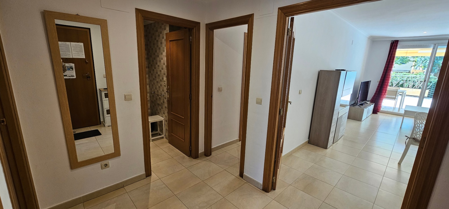 Couloir d'entrée avec sol en grès et menuiseries en bois, desservant le séjour lumineux et une salle de bain aux tons gris mosaïque.