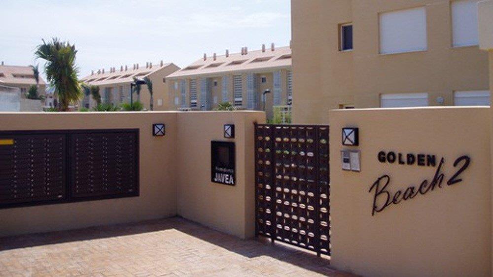 Entrée principale du complexe Golden Beach 2, avec des murs ton sable, des boîtes aux lettres intégrées et un portail en métal sombre.