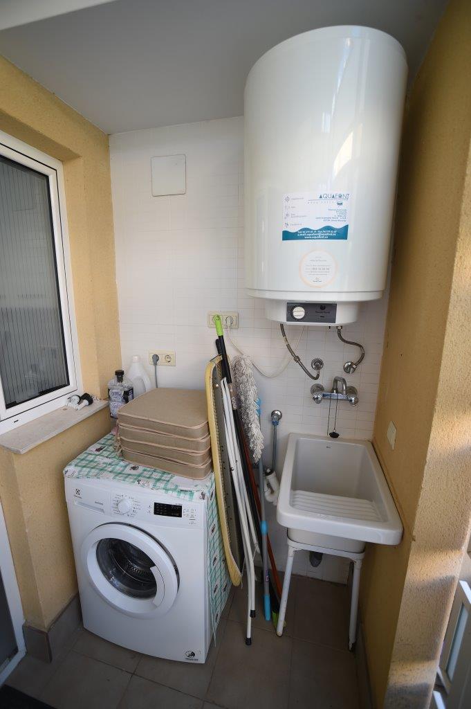 Espace buanderie couvert comprenant un lave-linge, un grand chauffe-eau électrique et un évier de service pratique pour l'entretien.