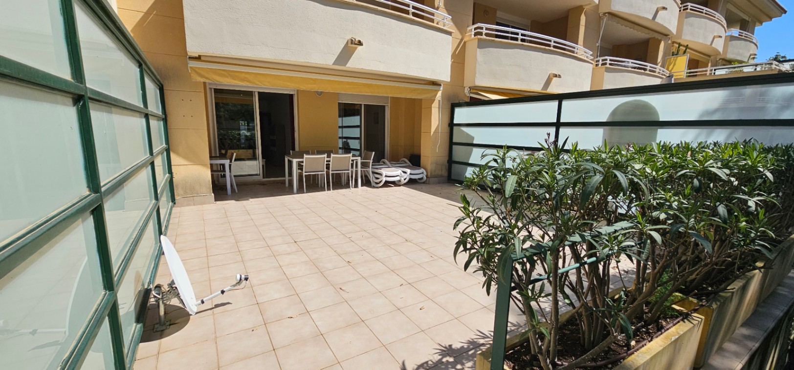 Grande terrasse en rez-de-chaussée avec carrelage clair, coin repas extérieur, chaises longues et parois d'intimité en verre dépoli.