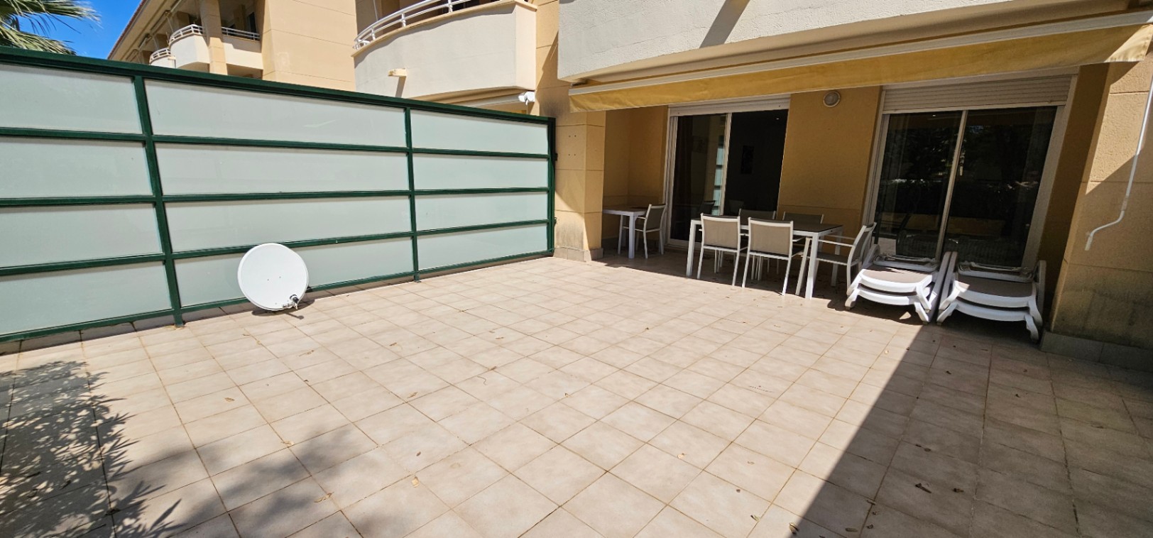 Grande terrasse en rez-de-chaussée avec carrelage clair, espace dînatoire abrité par un store banne et paroi de séparation translucide.