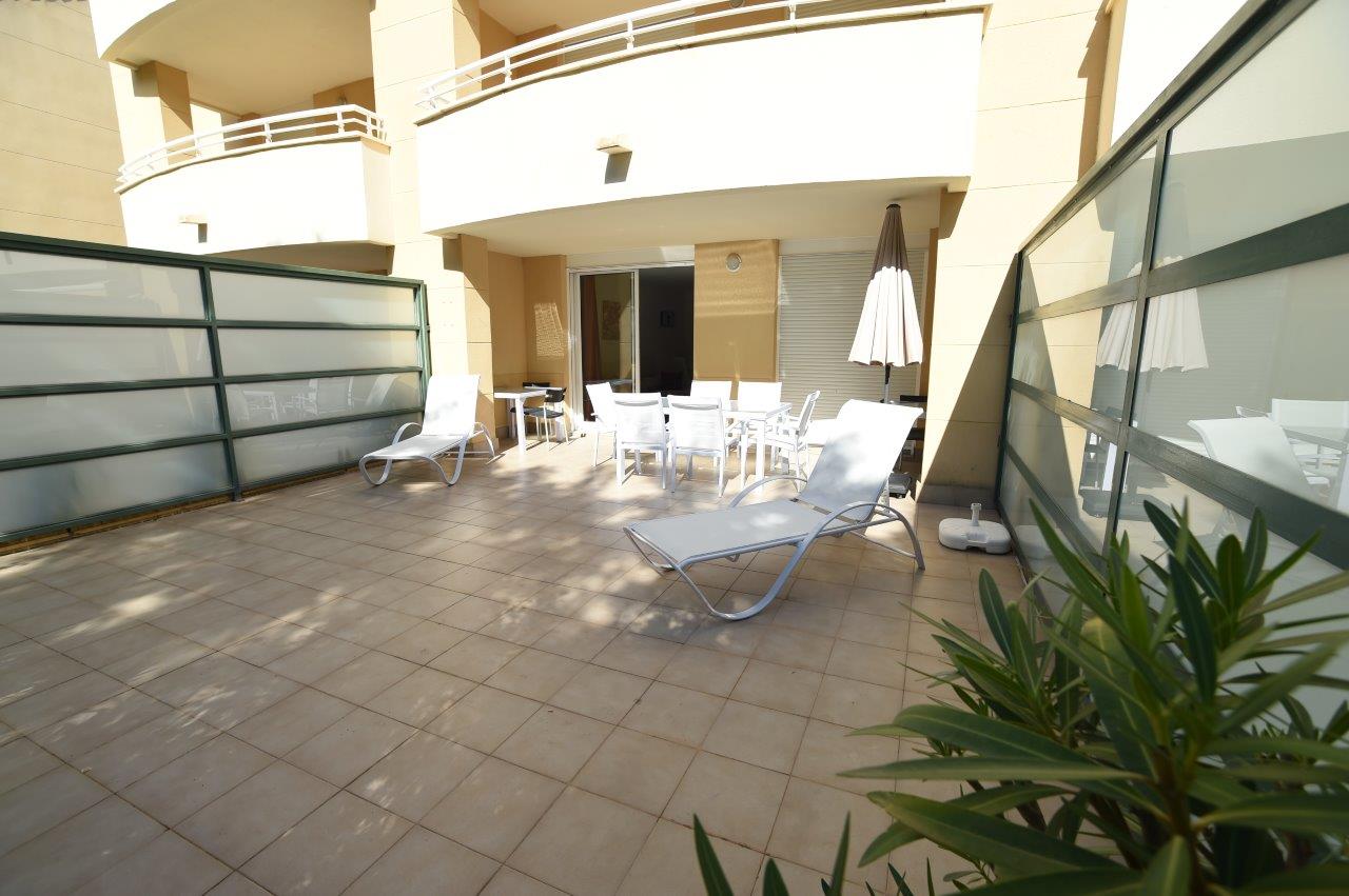 Terrasse privée au rez-de-chaussée avec carrelage au sol, équipée de chaises longues blanches et d'un coin repas extérieur abrité.