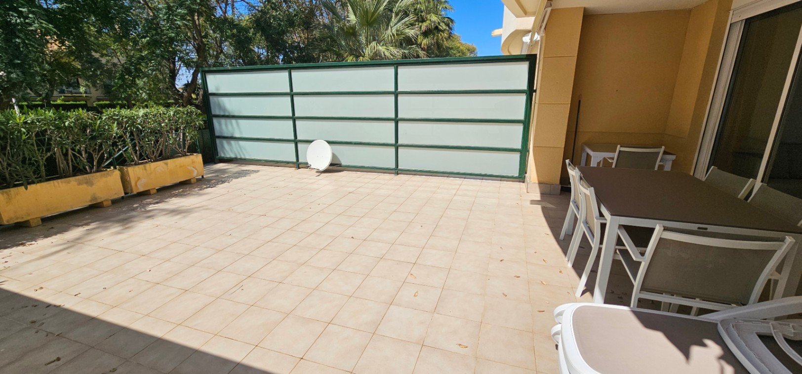 Terrasse privée avec revêtement en carrelage beige, coin repas extérieur ombragé et paroi de séparation en verre dépoli pour l'intimité.