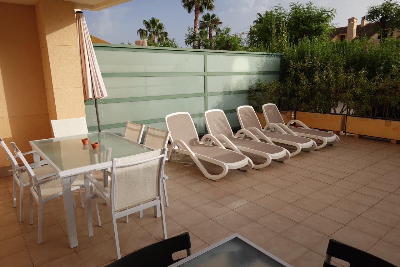 Terrasse privée dallée comprenant un coin repas extérieur et des bains de soleil, délimitée par une paroi en verre dépoli et des jardinières de lauriers.