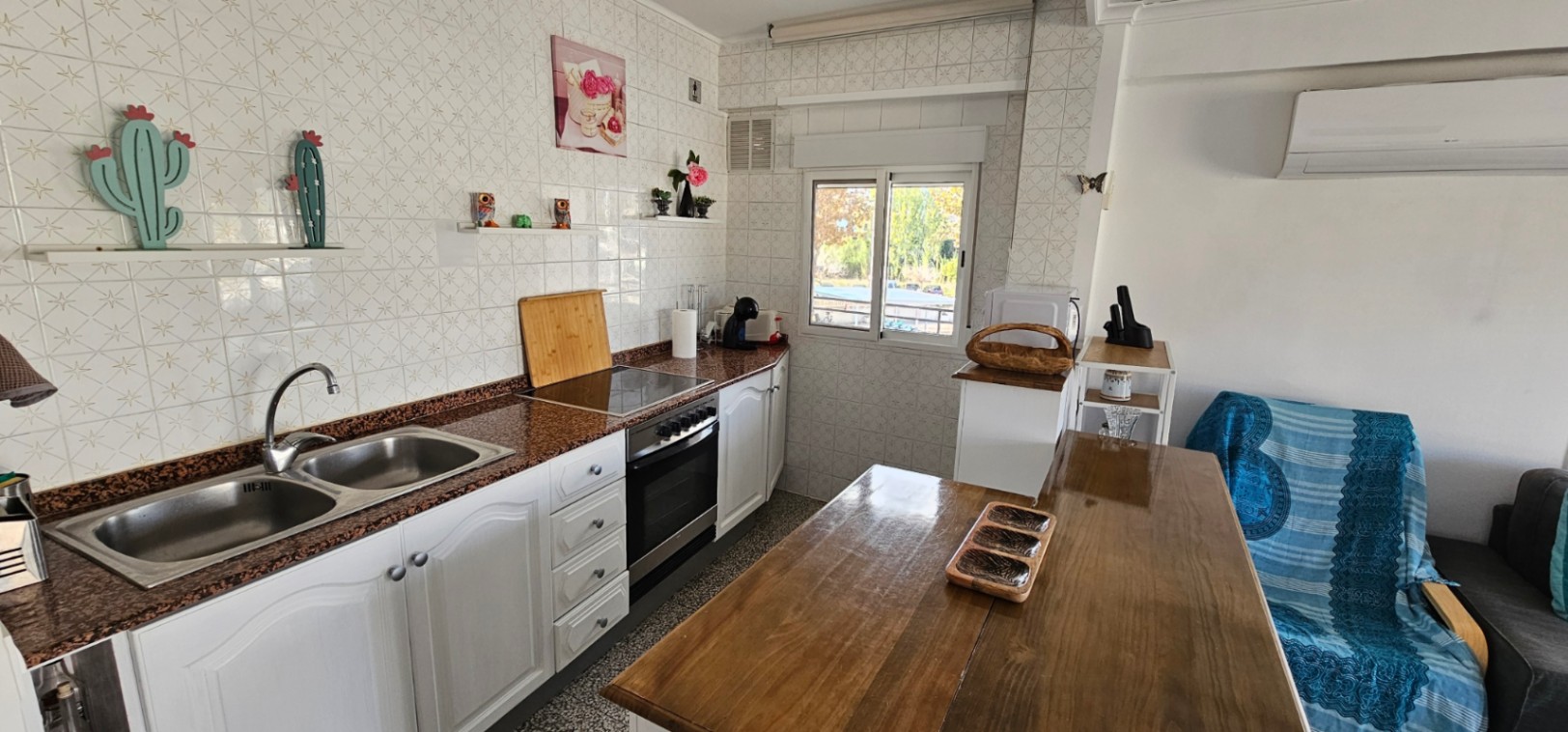 Cuisine ouverte avec plan de travail en granit, double évier et placards blancs. Comprend une table à manger en bois, la climatisation et une fenêtre lumineuse.