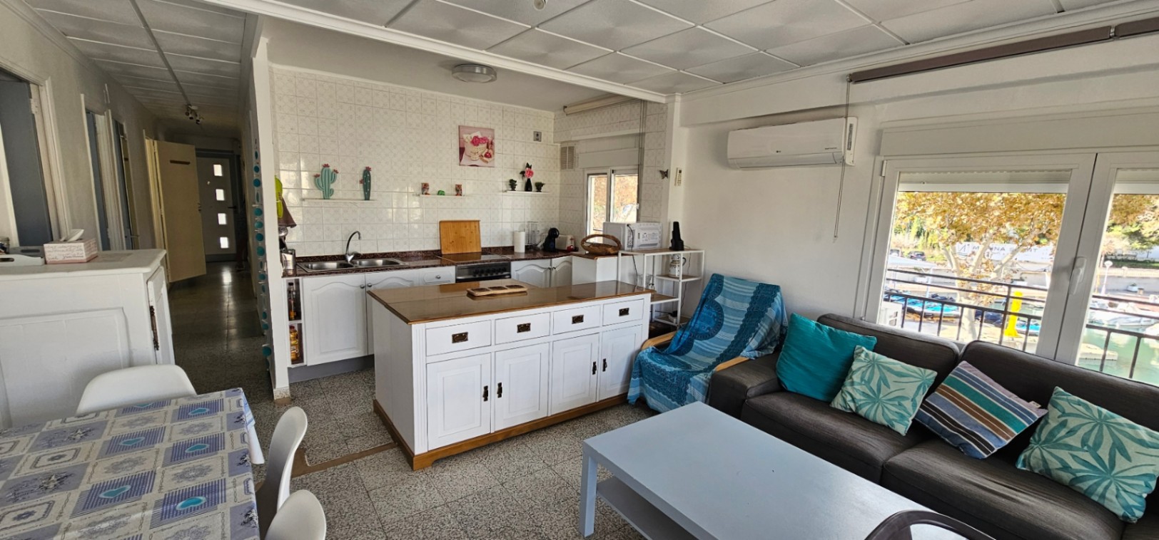 Espace de vie ouvert comprenant une cuisine avec îlot central, un salon confortable et de larges baies vitrées offrant une vue sur le port.